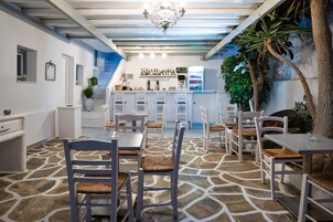 Um restaurante com mobiliário branco, piso de pedra e um espaço de bar com prateleiras cheias de garrafas.