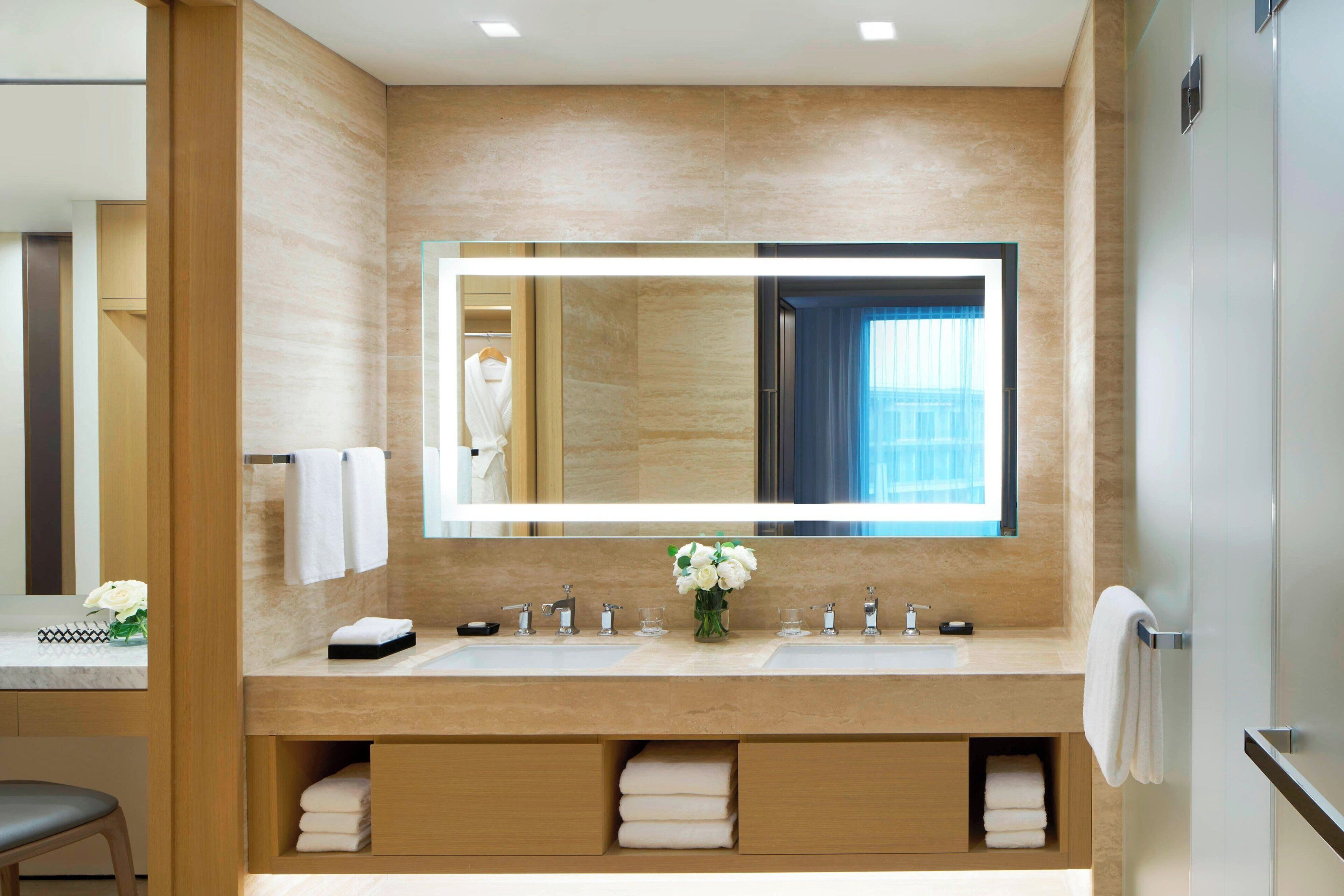 A modern bathroom with a large mirror, two sinks, and a vanity with storage.
