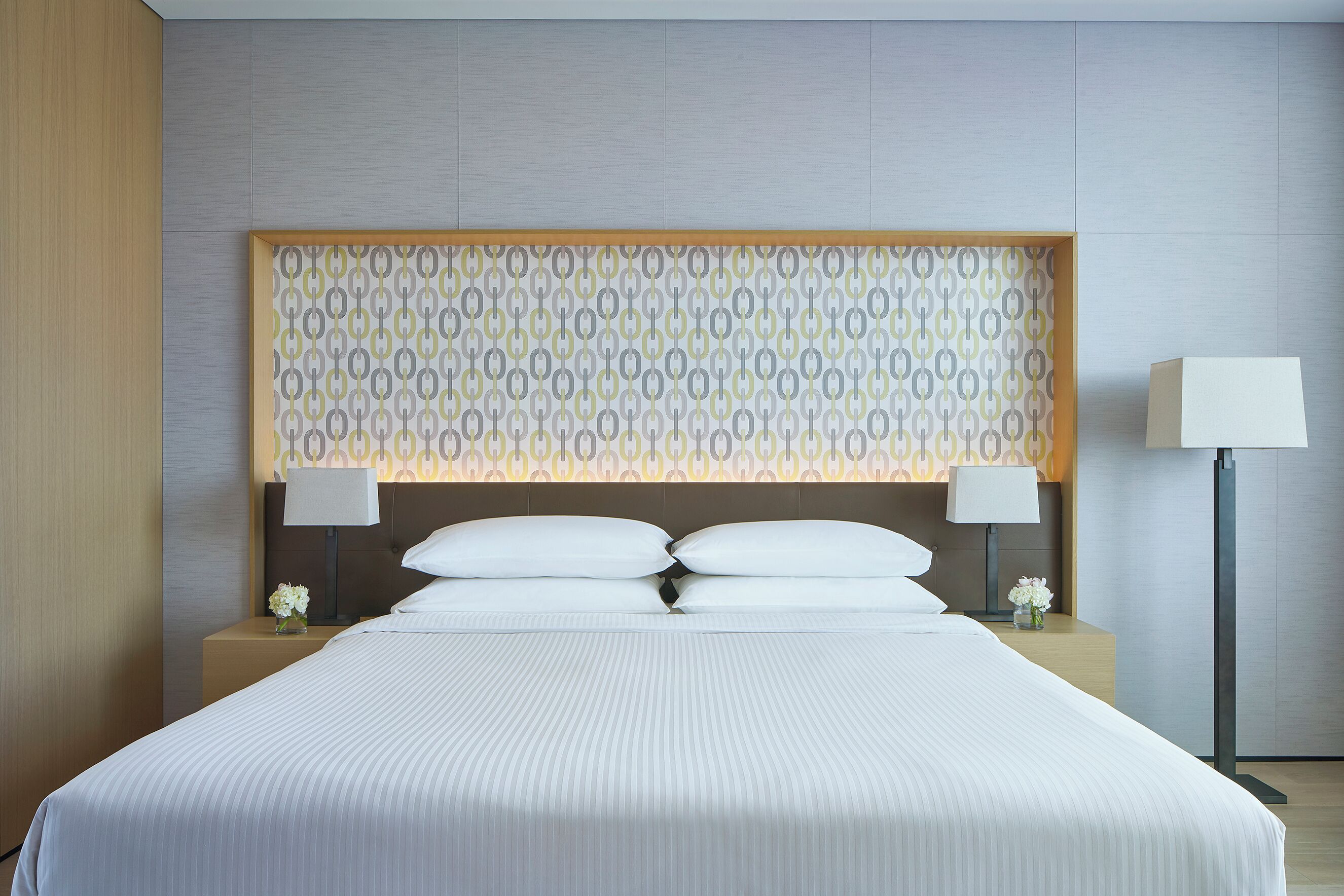 A neatly made bed with white linens, two bedside tables with lamps, and a patterned headboard.