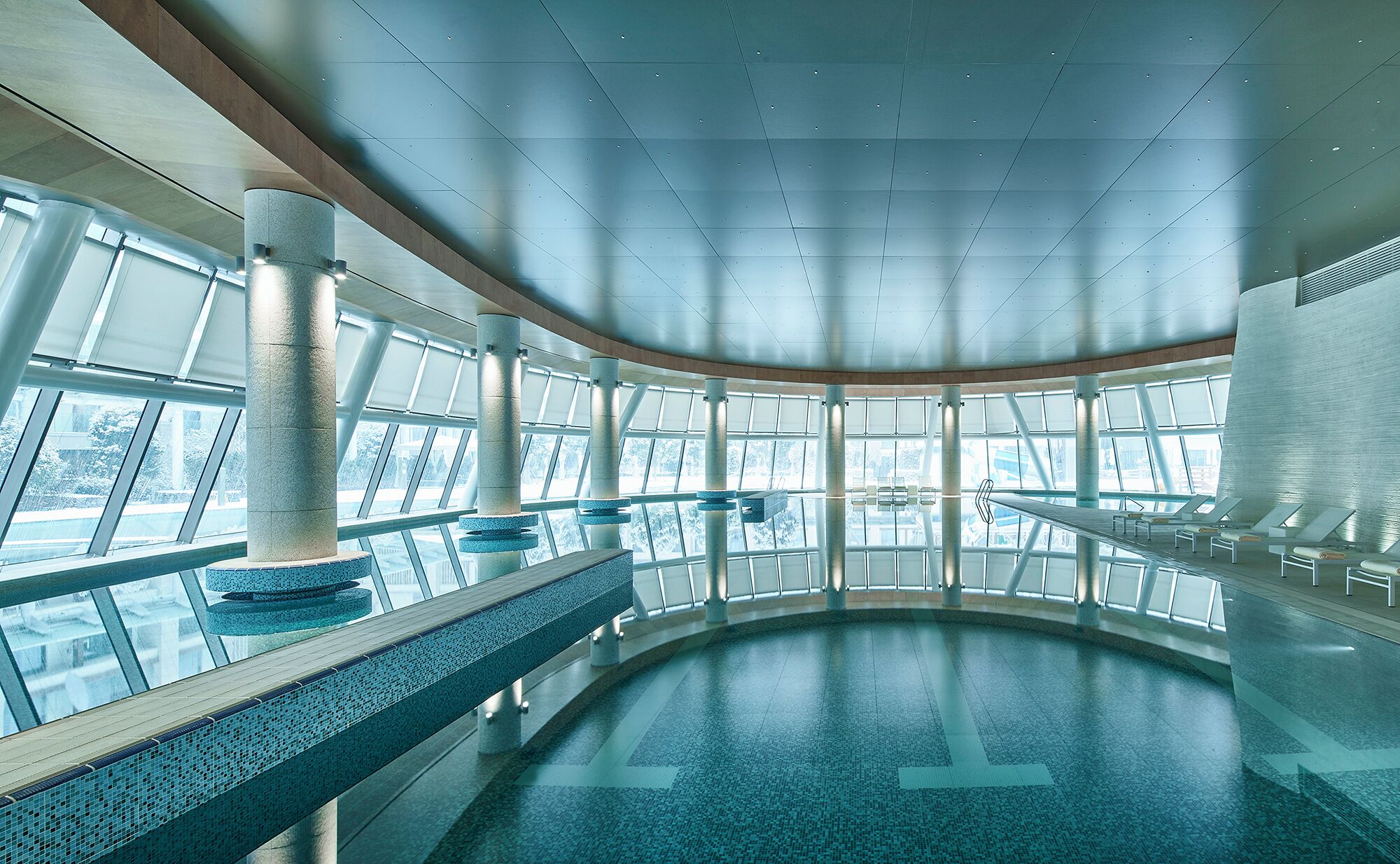 A spacious indoor swimming pool with clear glass walls, large windows, and a modern architectural design.
