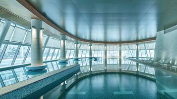 A spacious indoor swimming pool with clear glass walls, large windows, and a modern architectural design.