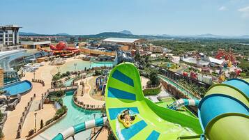 A water park with a large green water slide, a pool area, and a mountainous backdrop.