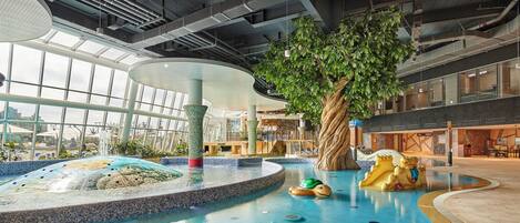 An indoor pool area with a central tree, a water feature, and a seating area.