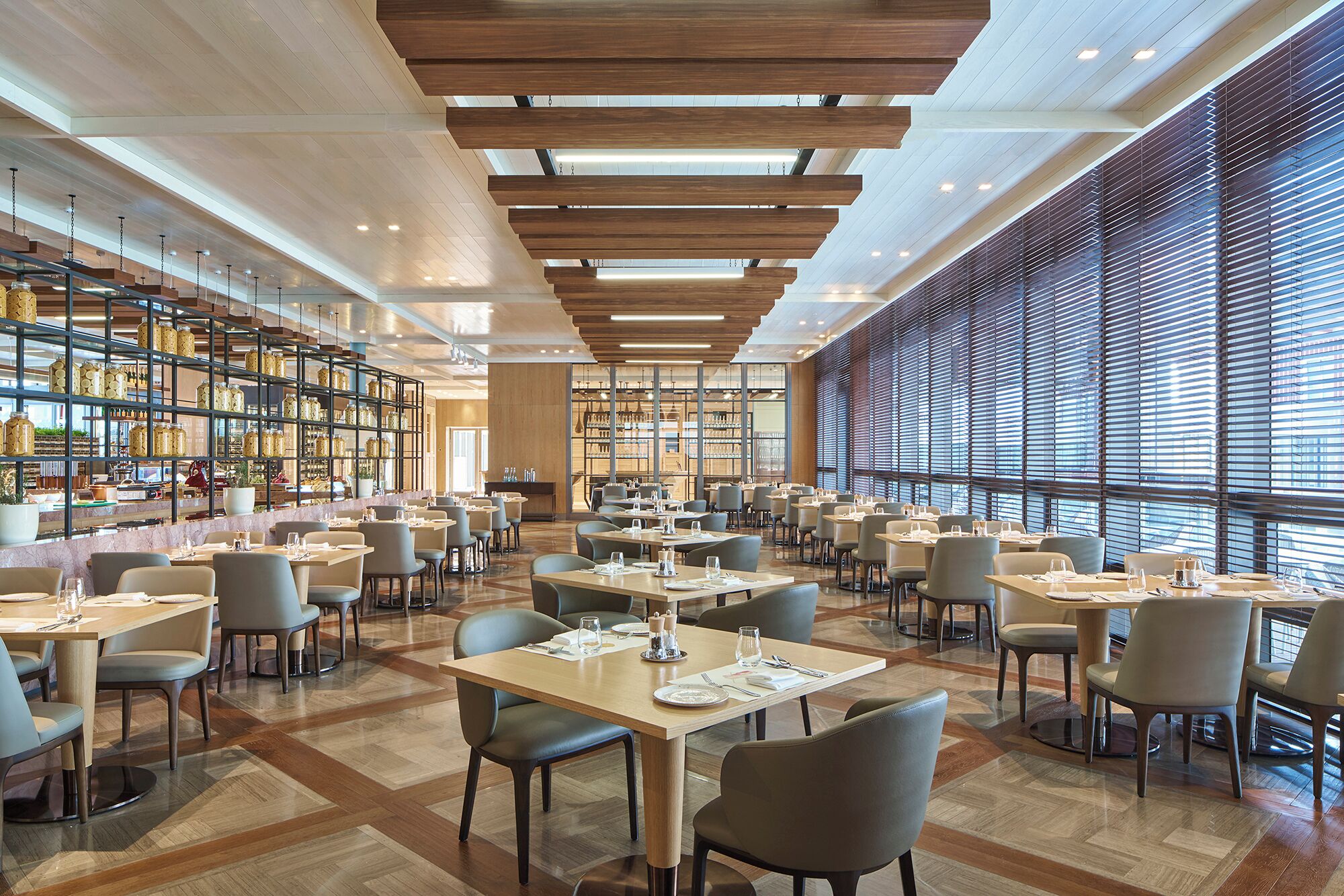 A spacious restaurant with high ceilings, wooden beams, and large windows. Tables are neatly arranged with chairs.