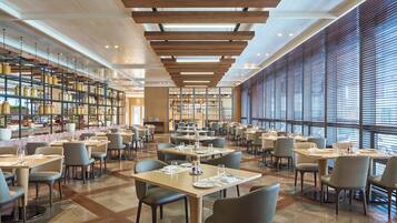 A spacious restaurant with high ceilings, wooden beams, and large windows. Tables are neatly arranged with chairs.