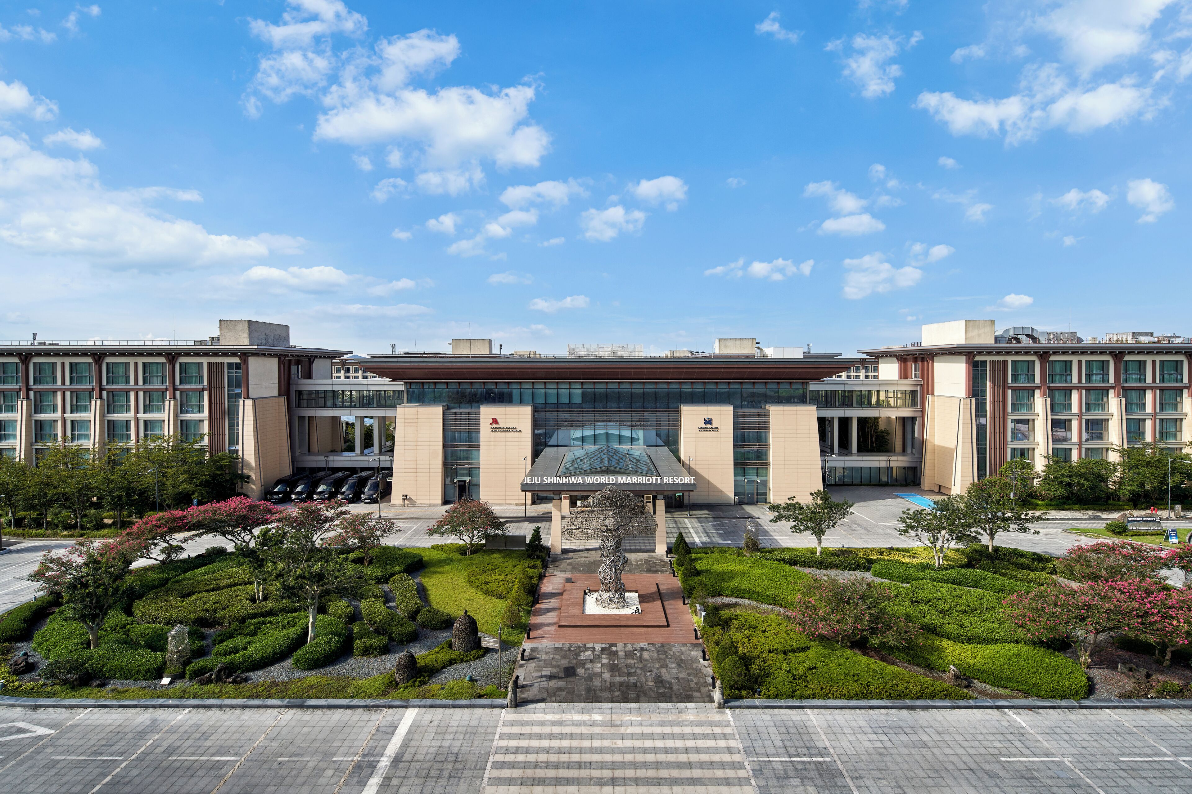 A modern hotel with a central courtyard, a large entrance, and a parking area.