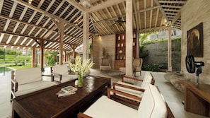 A spacious indoor area with a high ceiling, wooden beams, and a view of a landscaped garden.