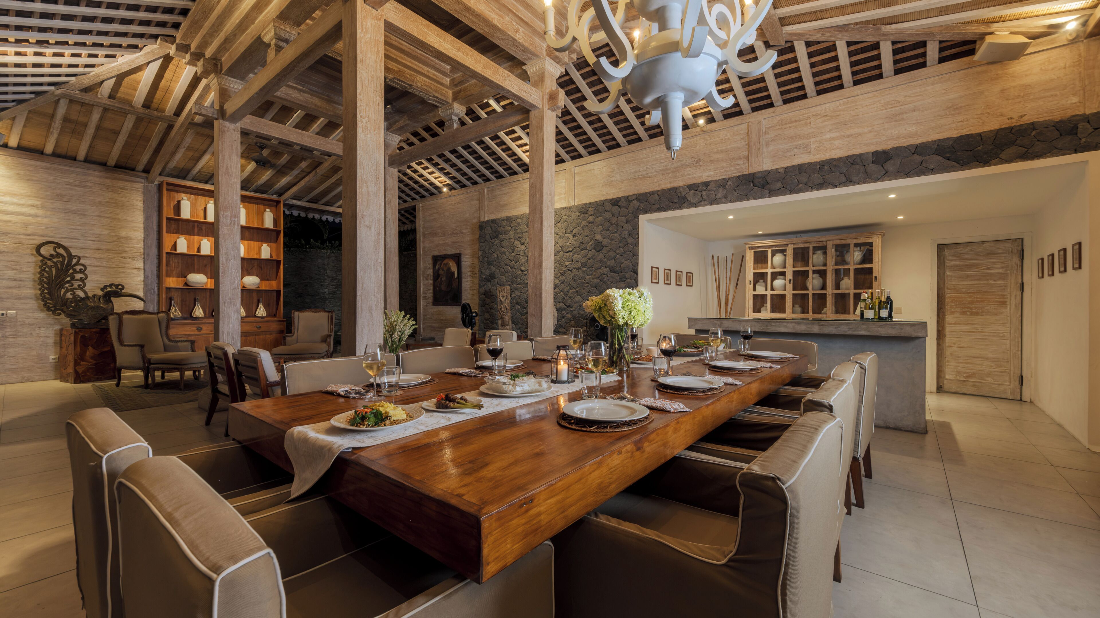 A spacious dining area with a long wooden table, multiple chairs, and a stone accent wall.