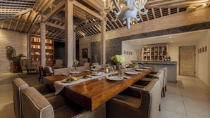 A spacious dining area with a long wooden table, multiple chairs, and a stone accent wall. - Villa Mannao by Villa Finder (Kerobokan)