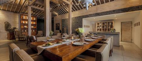A spacious dining area with a long wooden table, multiple chairs, and a stone accent wall.