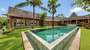 A swimming pool with a tiled edge, surrounded by a well-maintained lawn and tropical plants. - Villa Mannao by Villa Finder (Kerobokan)