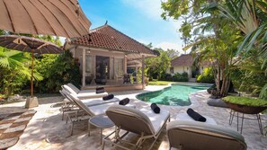 Un área junto a la piscina con sillones de descanso, una zona de estar cubierta y una piscina.