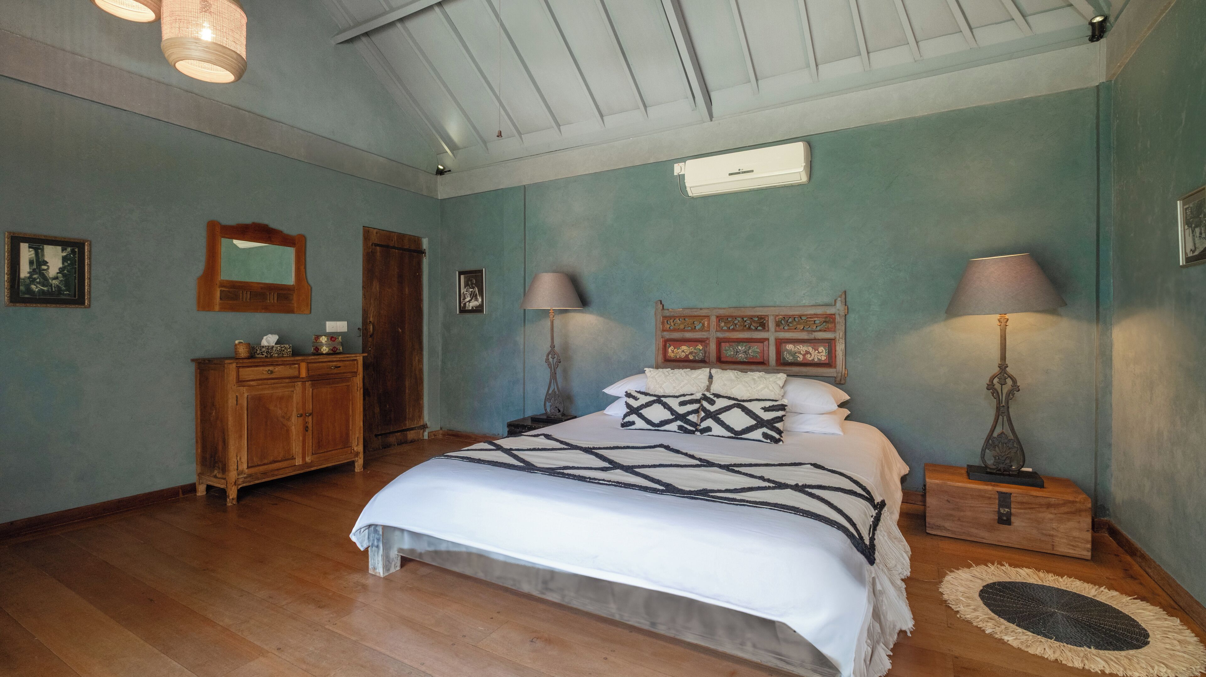 Un dormitorio con una cama de madera, dos mesitas de noche con lámparas, un aparador de madera, un espejo y un ventilador de techo.
