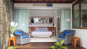 Un dormitorio con una cama, dos sillas de mimbre, una mesa de madera y vistas a un balcón.