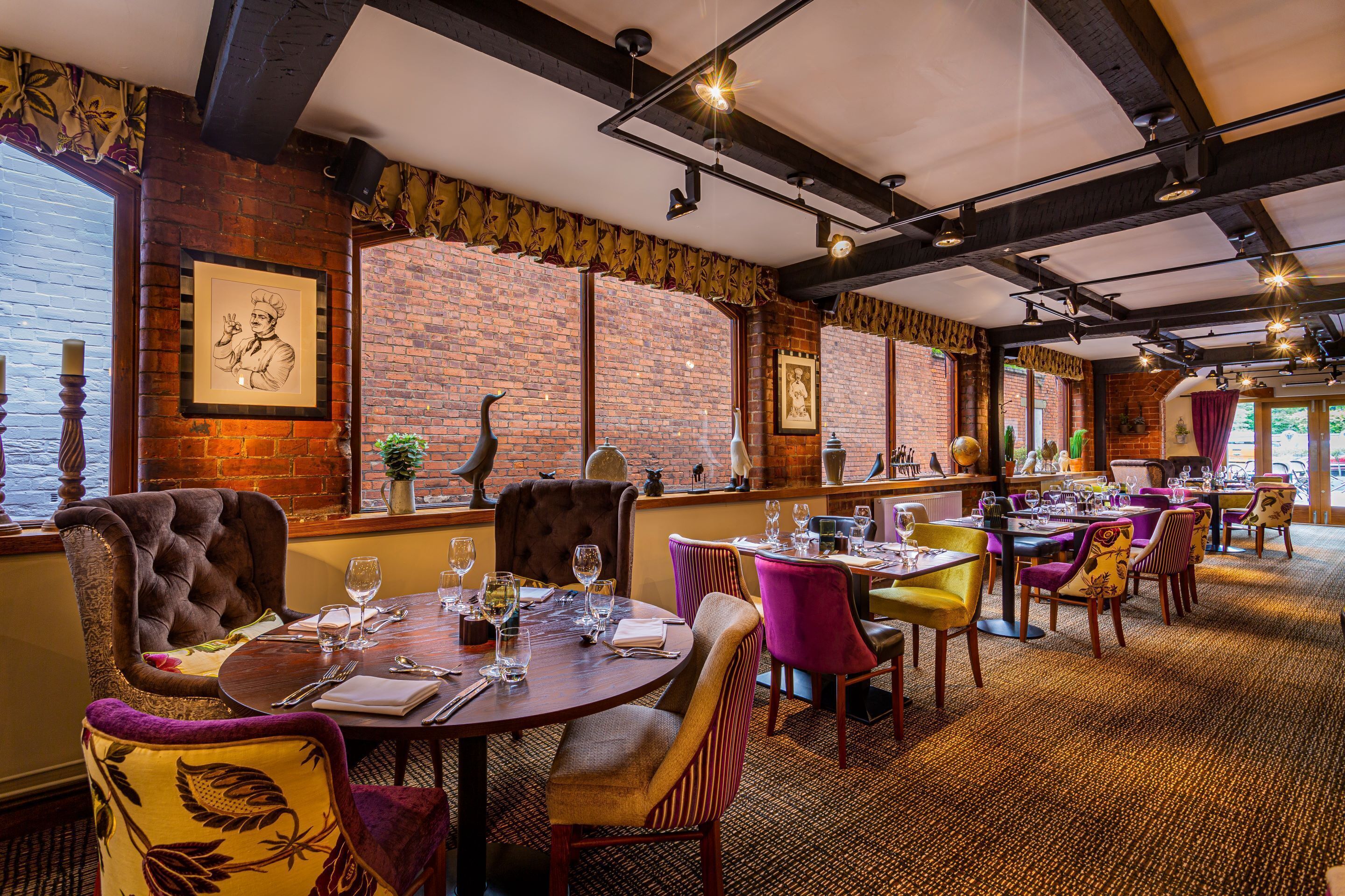 A restaurant with brick walls, exposed beams, and a variety of seating including plush chairs and tables set for dining.