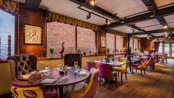 A restaurant with brick walls, exposed beams, and a variety of seating including plush chairs and tables set for dining.