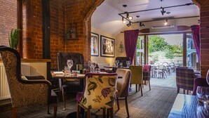 A restaurant with brick walls, wooden furniture, and a view through an archway. - The Feathers Hotel, Ledbury, Herefordshire (Ledbury)