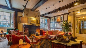 A cozy room with a fireplace, plush seating, and a large window offering a view of the street. - The Feathers Hotel, Ledbury, Herefordshire (Ledbury)
