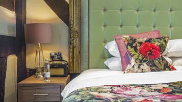 A neatly made bed with a floral duvet, a green upholstered headboard, and a bedside table with a lamp and a radio.