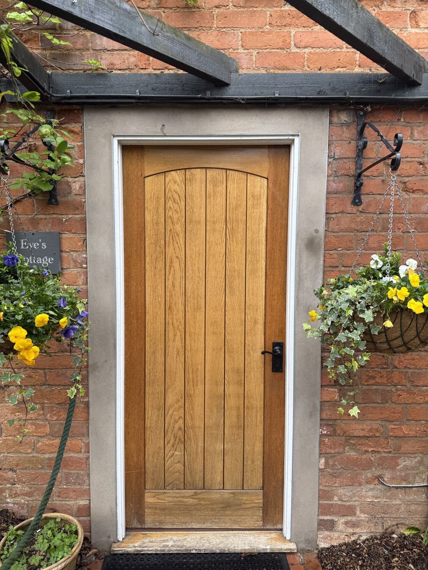 A wooden door with a metal handle, a brick wall, and hanging flower baskets.
