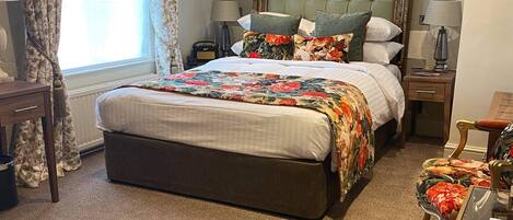 A bedroom with a large bed, floral-patterned curtains, a tufted headboard, and a carpeted floor.