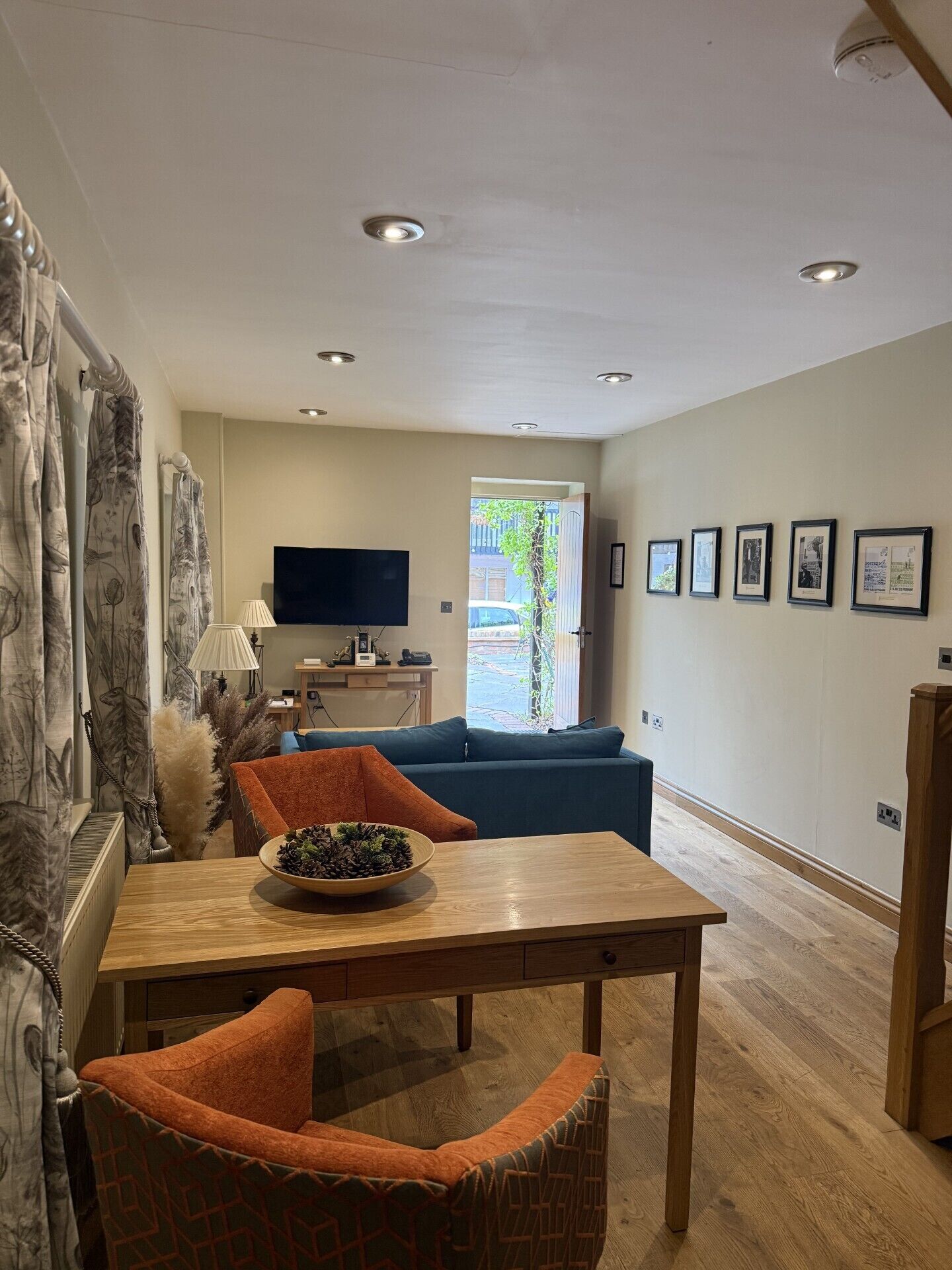 A living room with a television, a sofa, a dining table with a bowl, and a patterned chair.