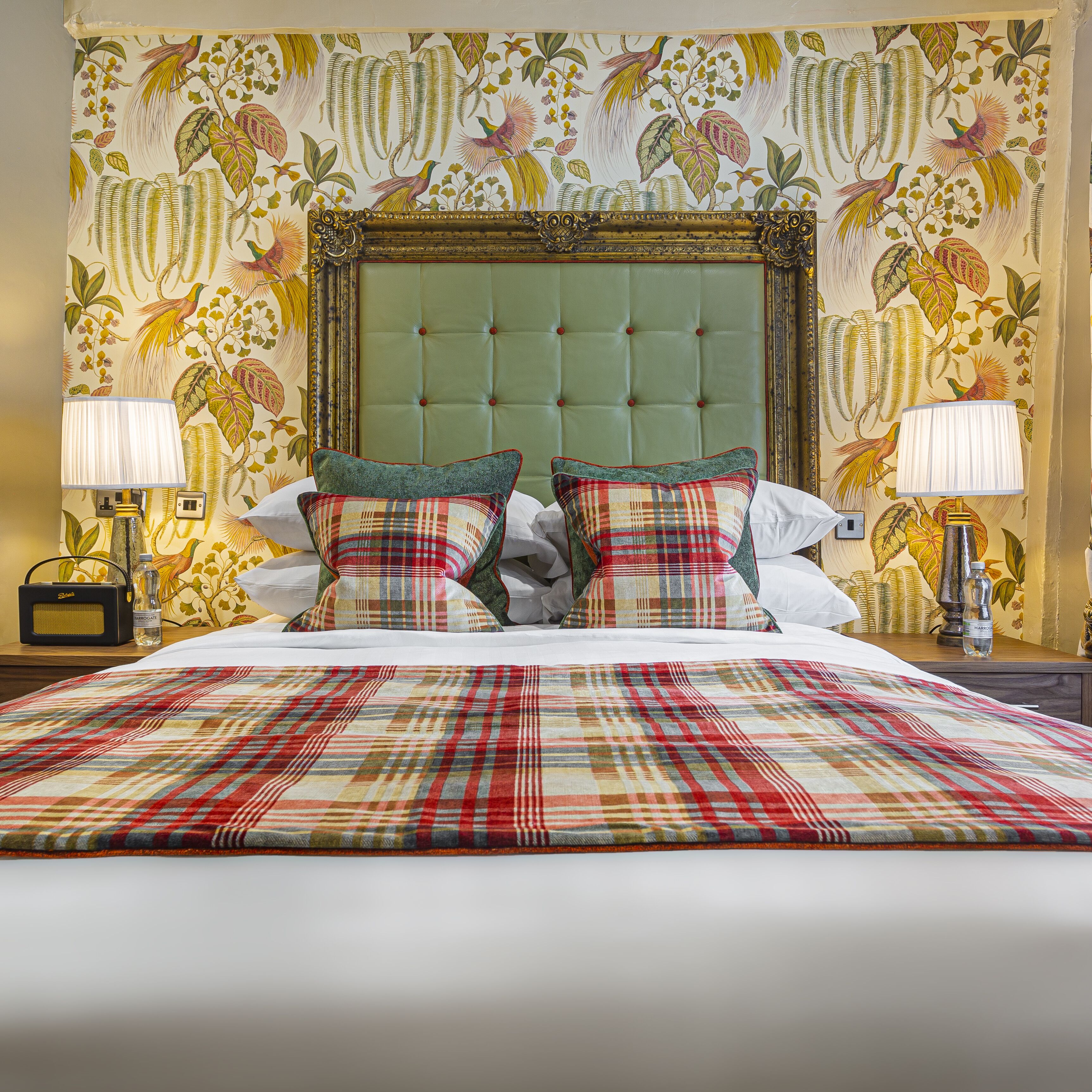 A hotel room with a large bed, two nightstands, a radio, and a wall with a floral mural.