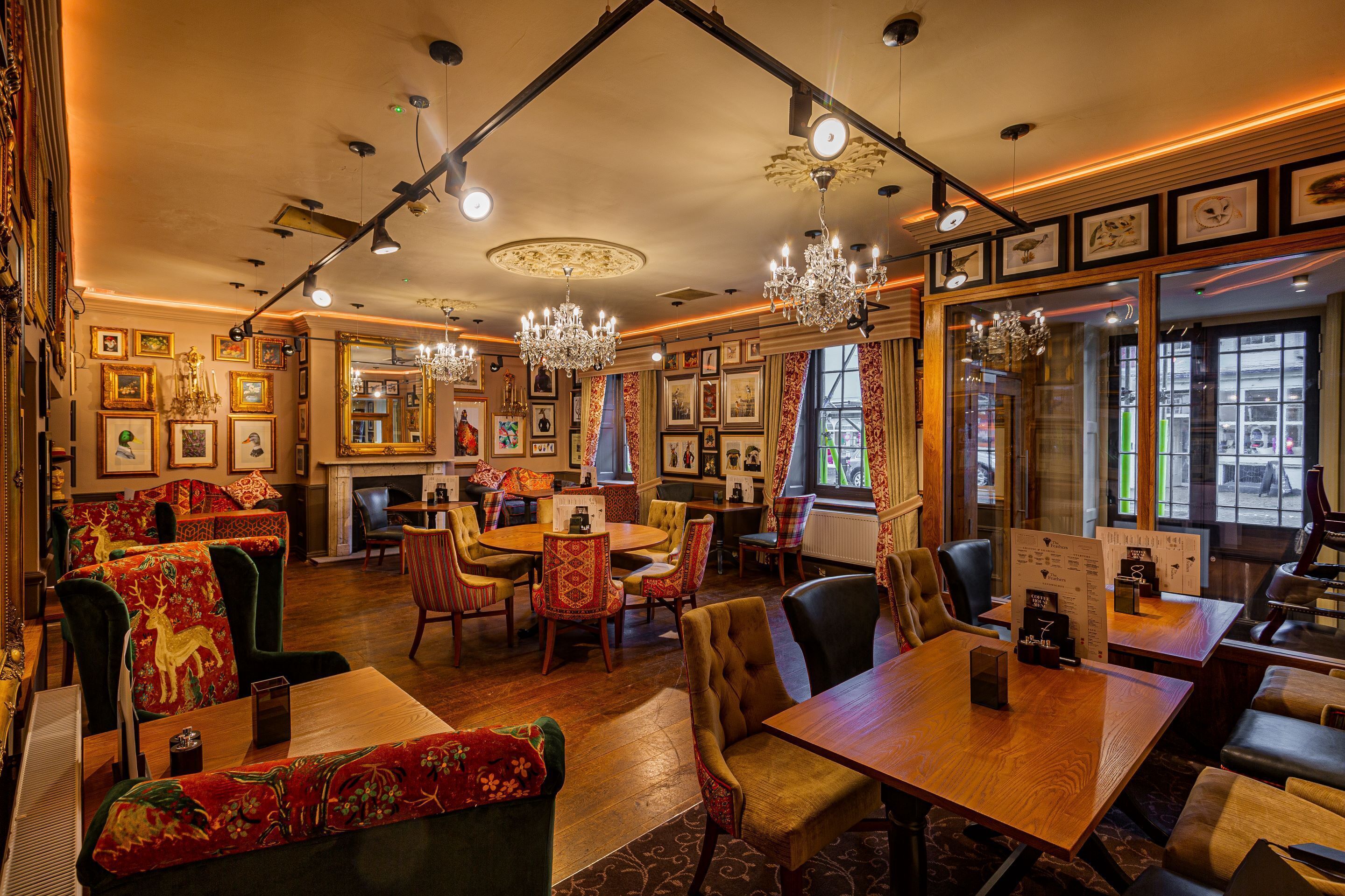 Un restaurant chaleureux avec des tables et des chaises en bois, un lustre et des tableaux encadrés aux murs.