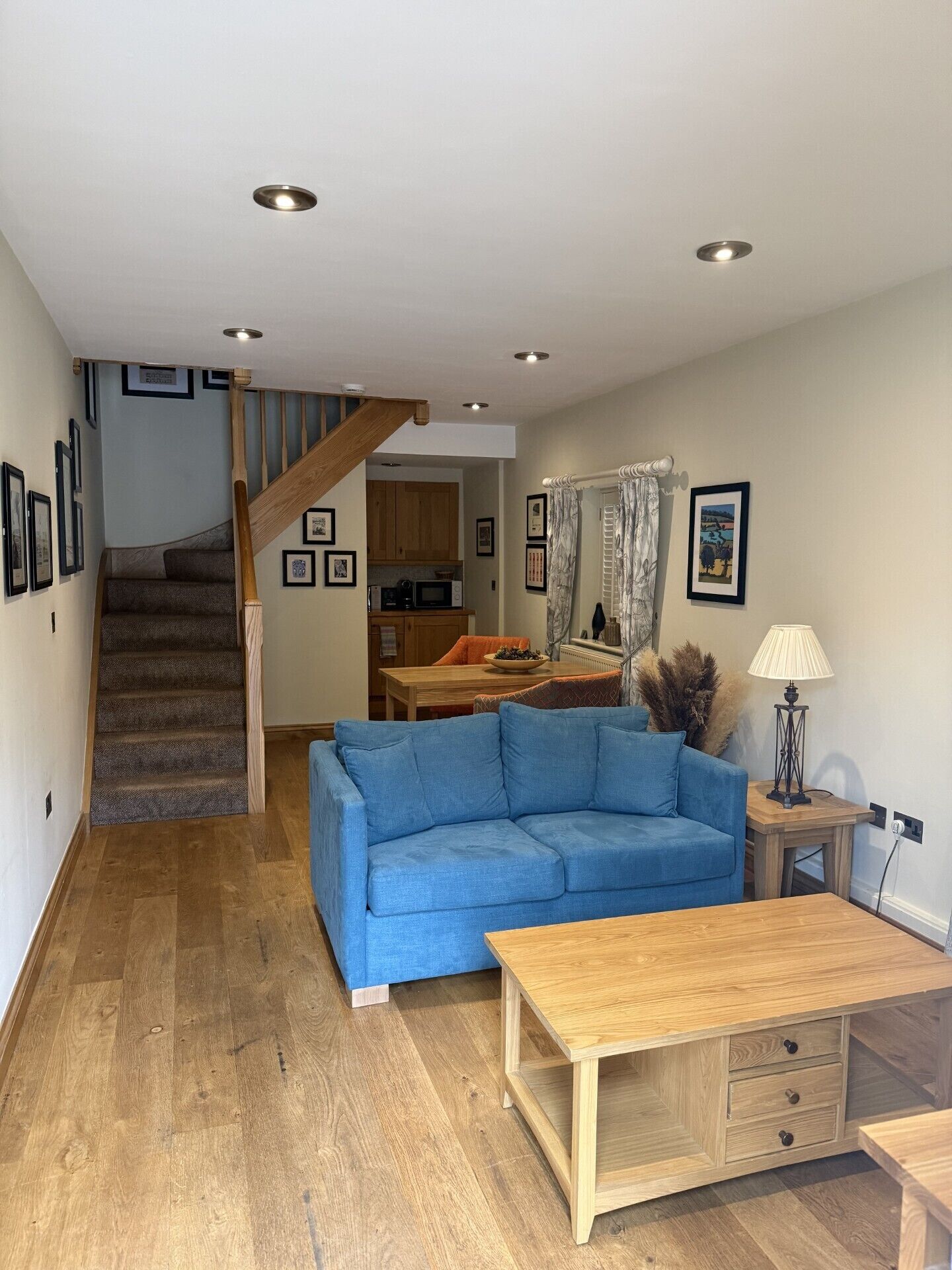 Una sala de estar con un sofá azul, una mesa de centro de madera y una escalera que conduce a una cocina.