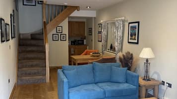 Una sala de estar con un sofá azul, una mesa de centro de madera y una escalera que conduce a una cocina.
