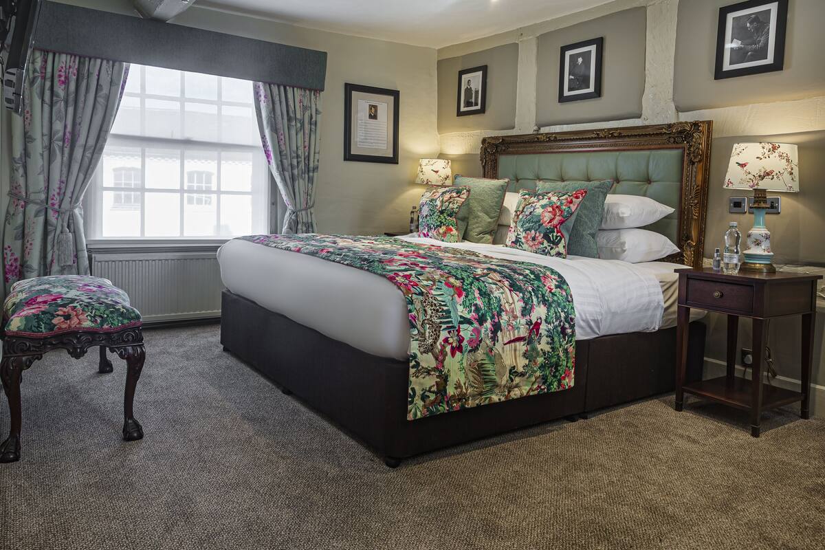 A neatly arranged bedroom with a large bed, a side table, a chair, and a window with curtains.