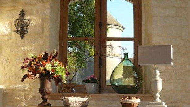 Ein Fenster mit Blick auf ein Haus, eine Vase mit Blumen, eine Lampe und ein Korb auf einem Holzboden.