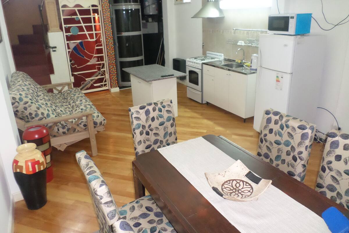 A compact living space with a dining area, kitchen, and a staircase leading to an upper level.