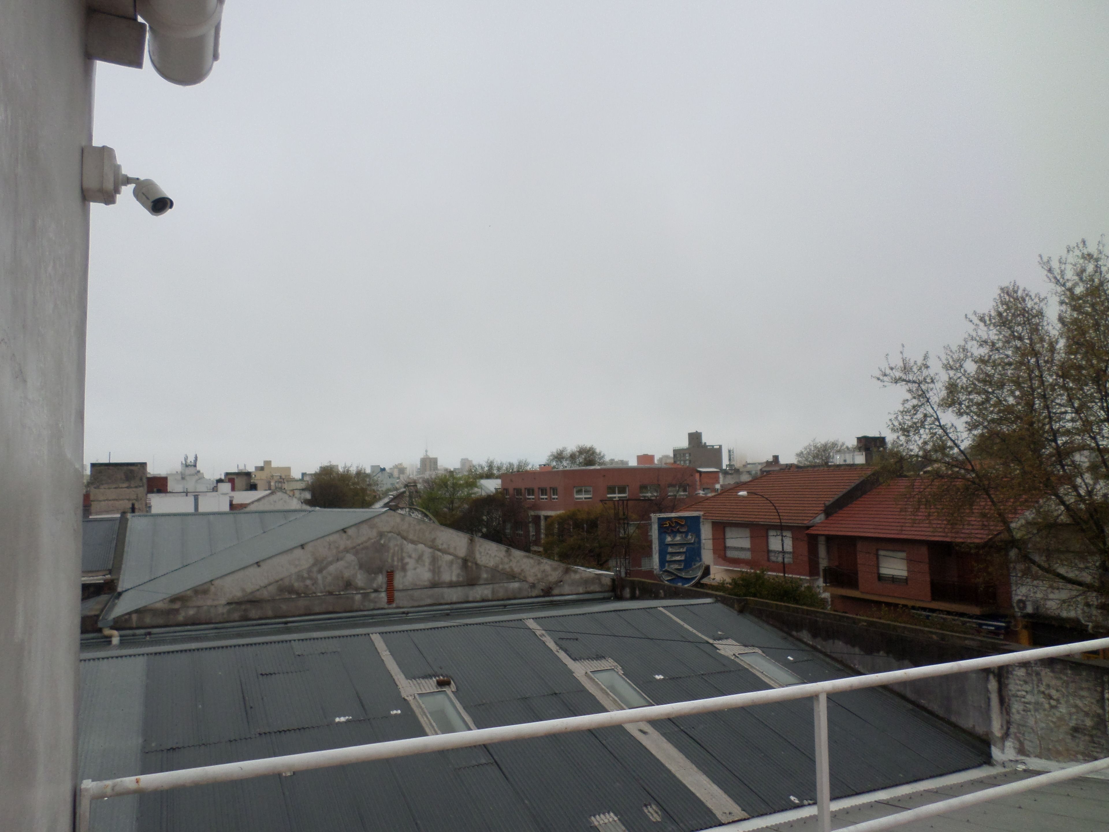A rooftop with a metal roof, a red building with a blue sign, and a view of a cityscape in the background.