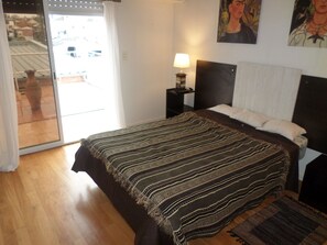 A bedroom with a bed, a nightstand, a lamp, and a painting on the wall. - Casas en MDQ Cordoba by EF (Mar del Plata)