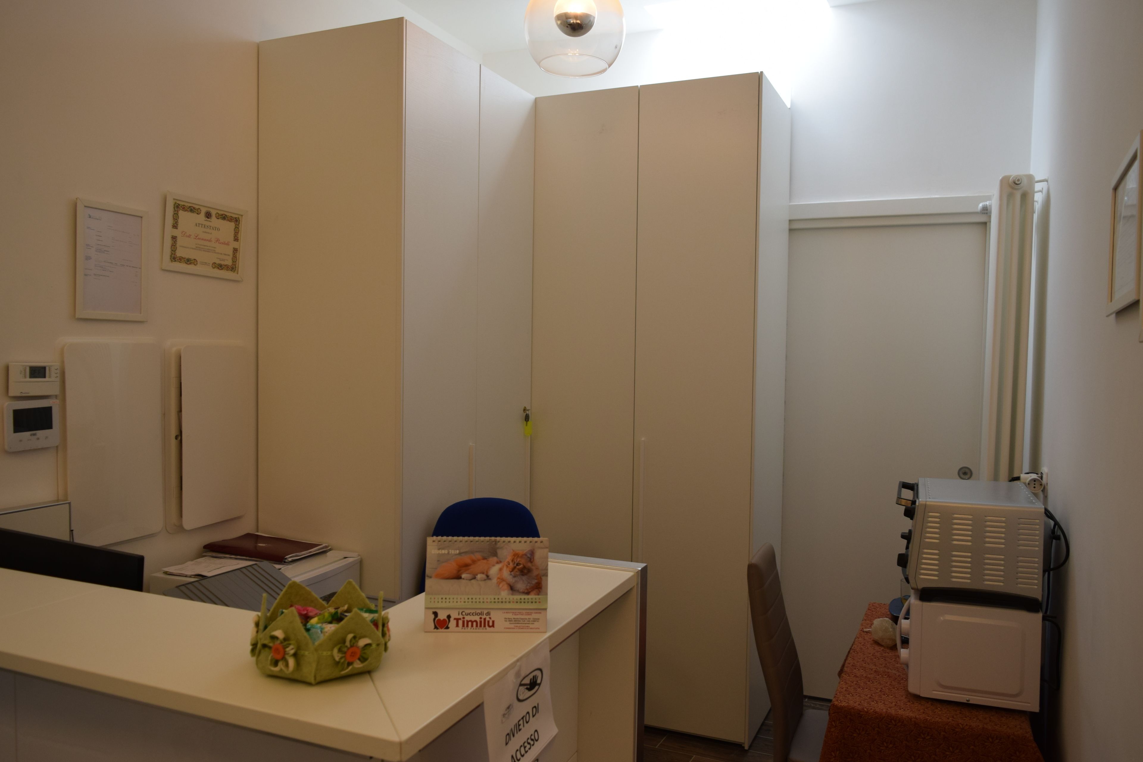 Mostrador de recepción con un letrero que indica acceso, un refrigerador pequeño y una silla.