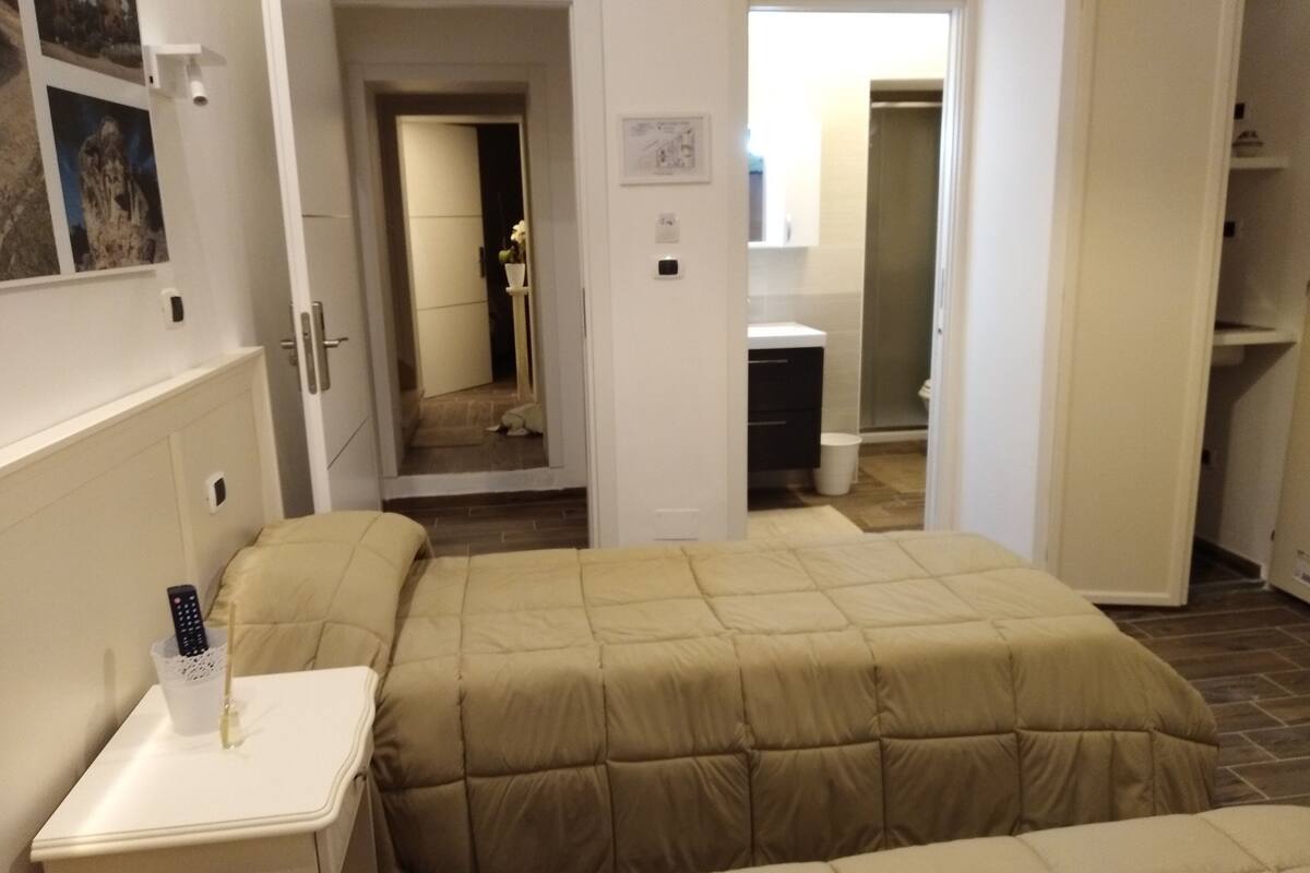A hotel room with a bed, a bedside table with a remote control, a mirror, and a bathroom visible through an open door.
