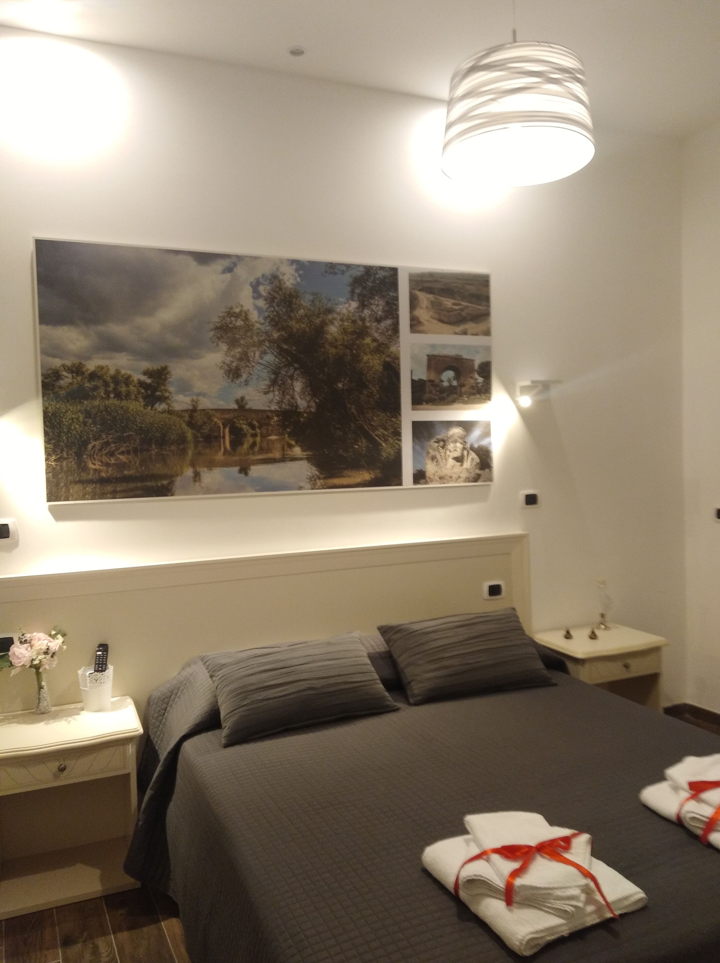 Quarto de hotel com uma cama, mesa de cabeceira, abajur e quadro na parede.