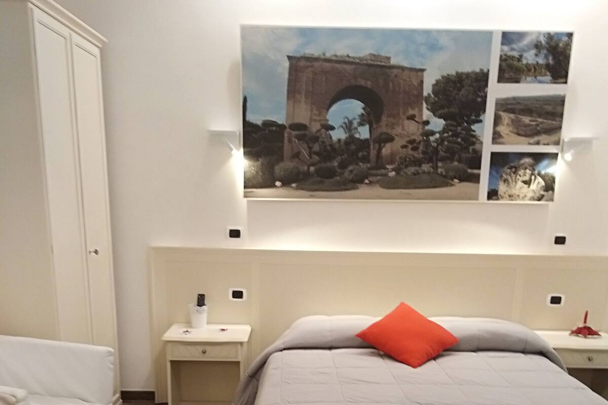 A bedroom with a bed, a nightstand, a bedside table, a chair, and a wooden floor.