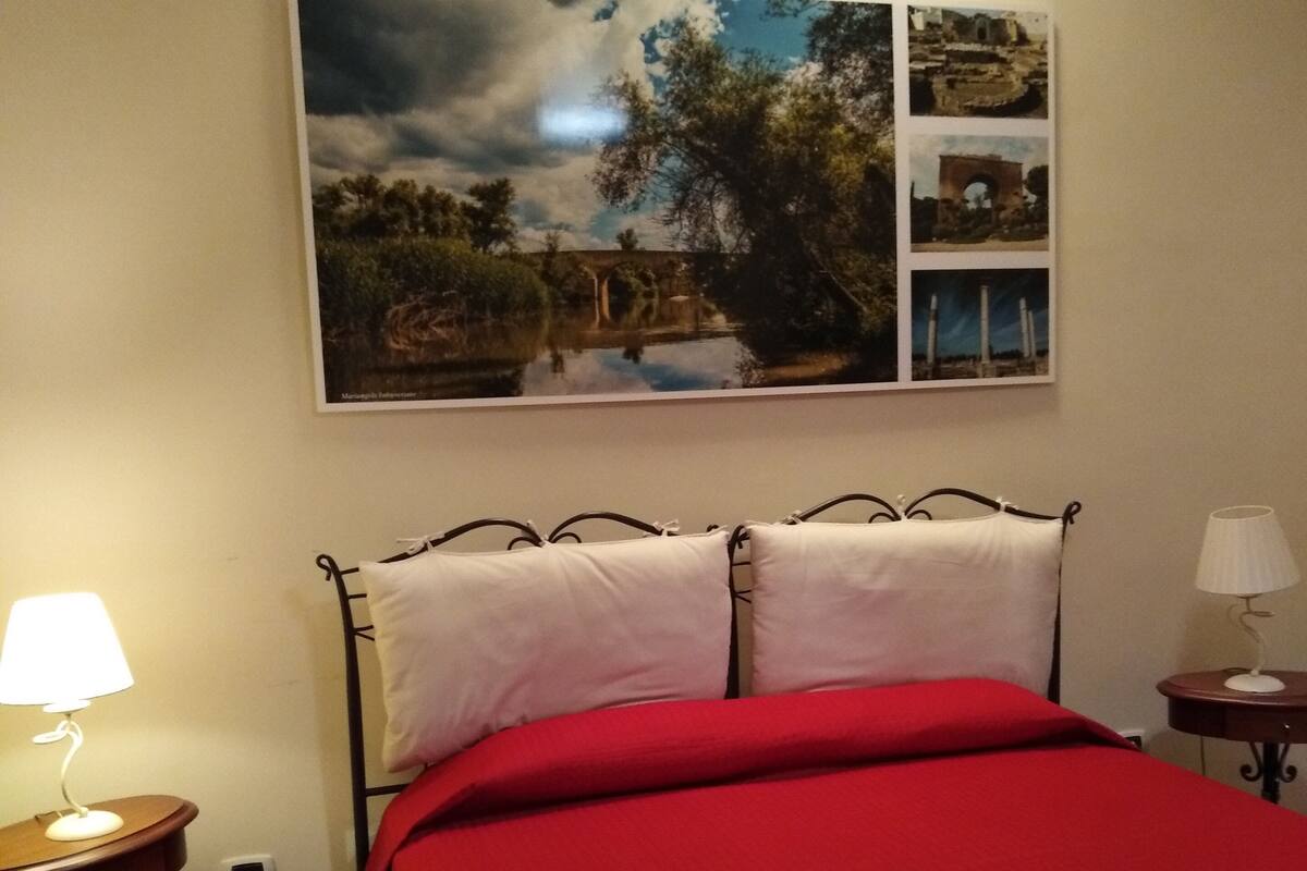 A bedroom with a bed, a nightstand, a lamp, and a wall-mounted picture.