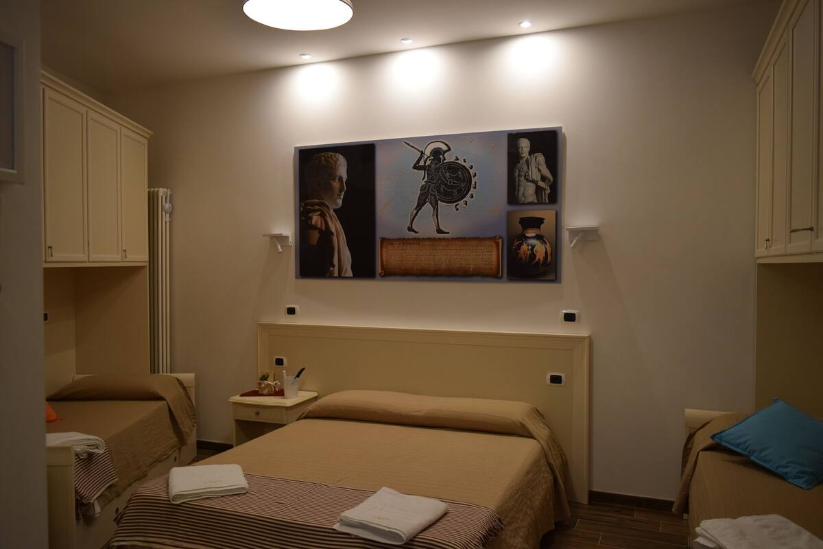 A hotel room with a bed, a nightstand, a chair, and artwork on the wall.
