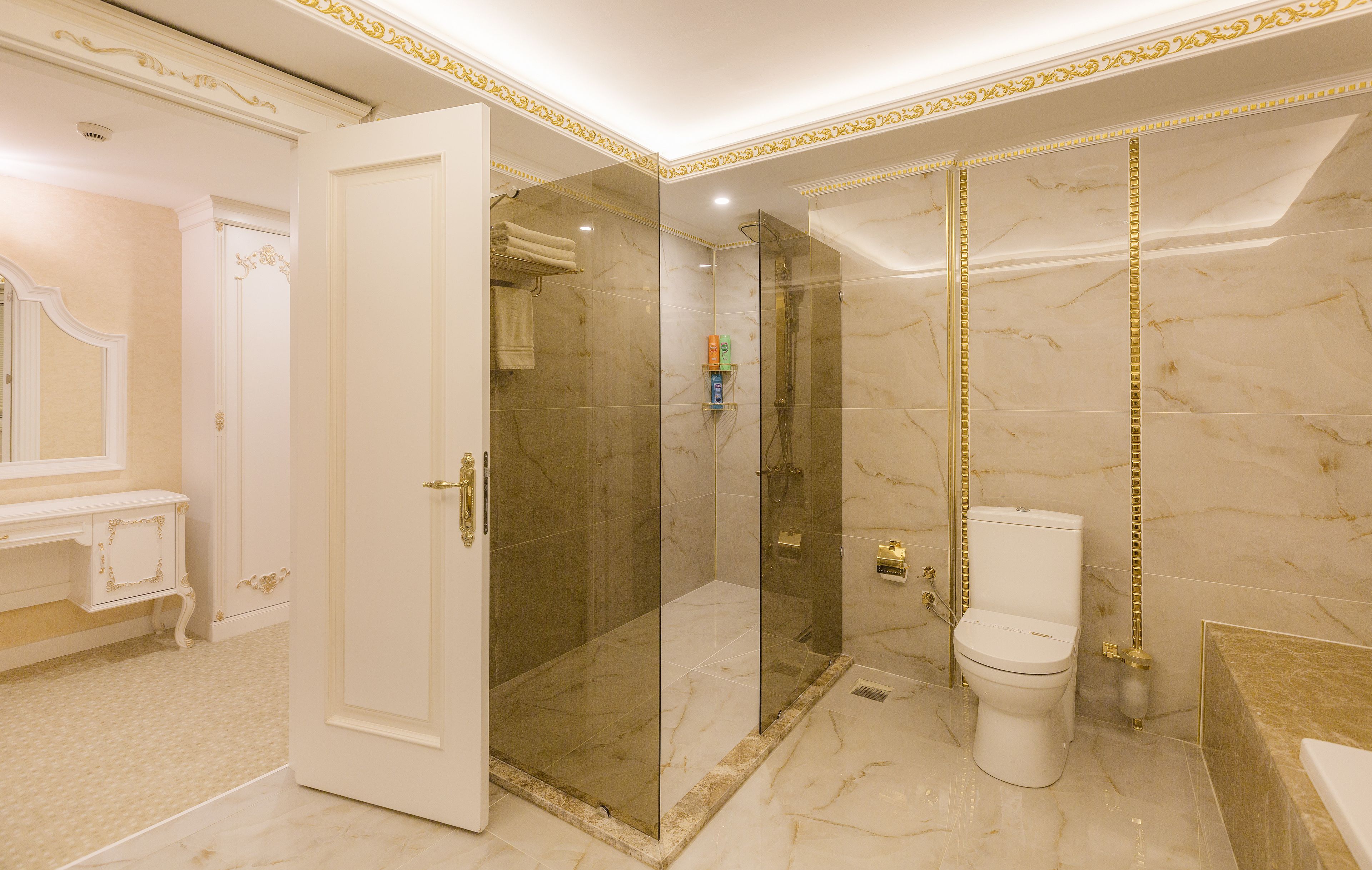 A luxurious bathroom with a marble floor, a glass-enclosed shower, a toilet, and a vanity with a mirror.