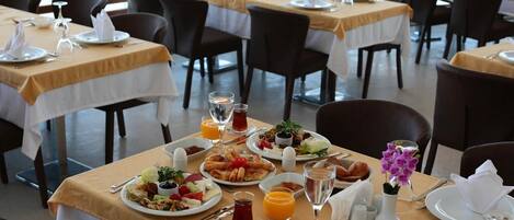 A dining area with tables set for breakfast, including plates of food, drinks, and cutlery.