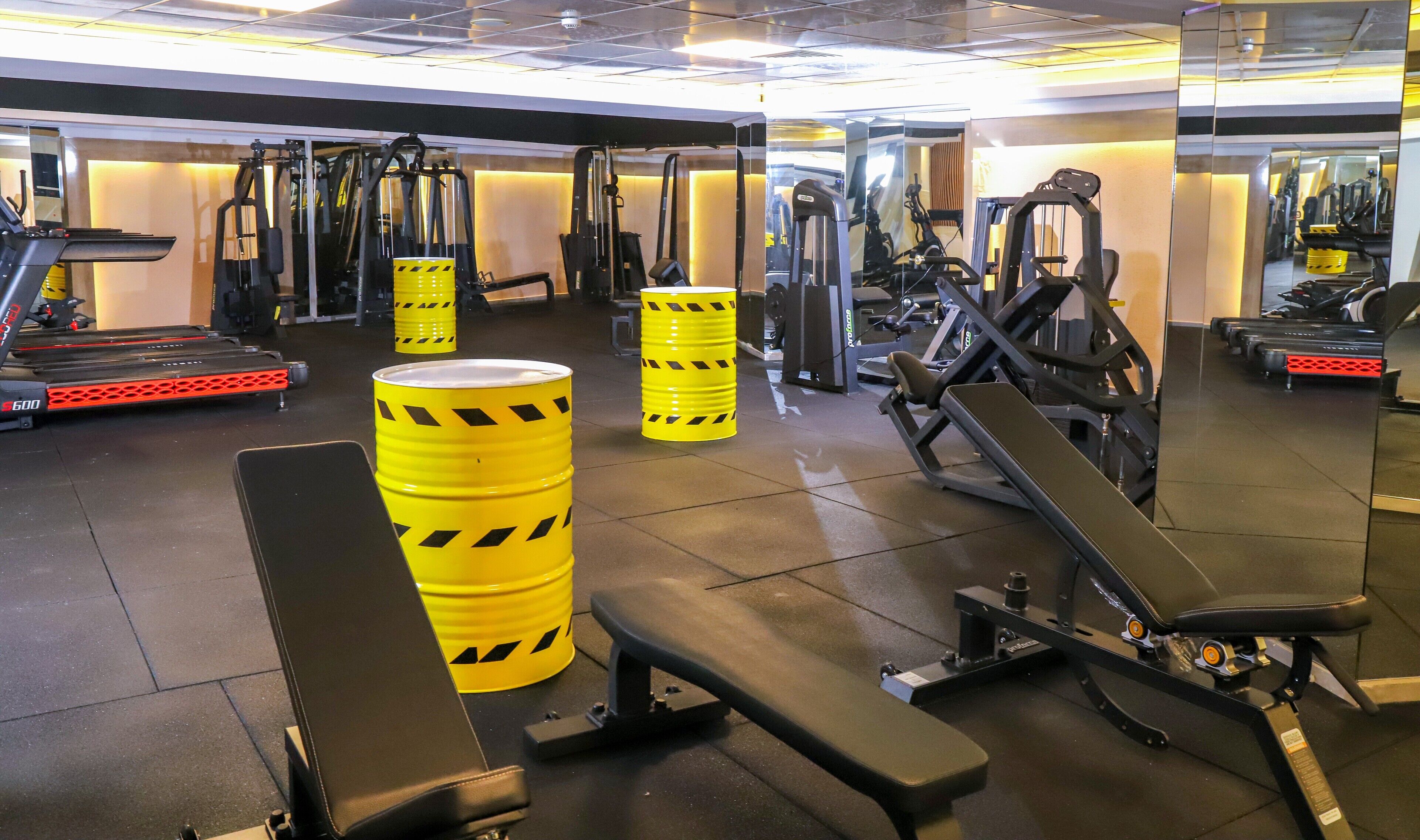 Ein Fitnessraum mit Trainingsgeräten, Bänken und gelben Barrels.