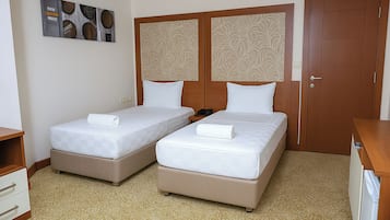 A hotel room with two beds, a wooden wardrobe, a desk, and a small cabinet.