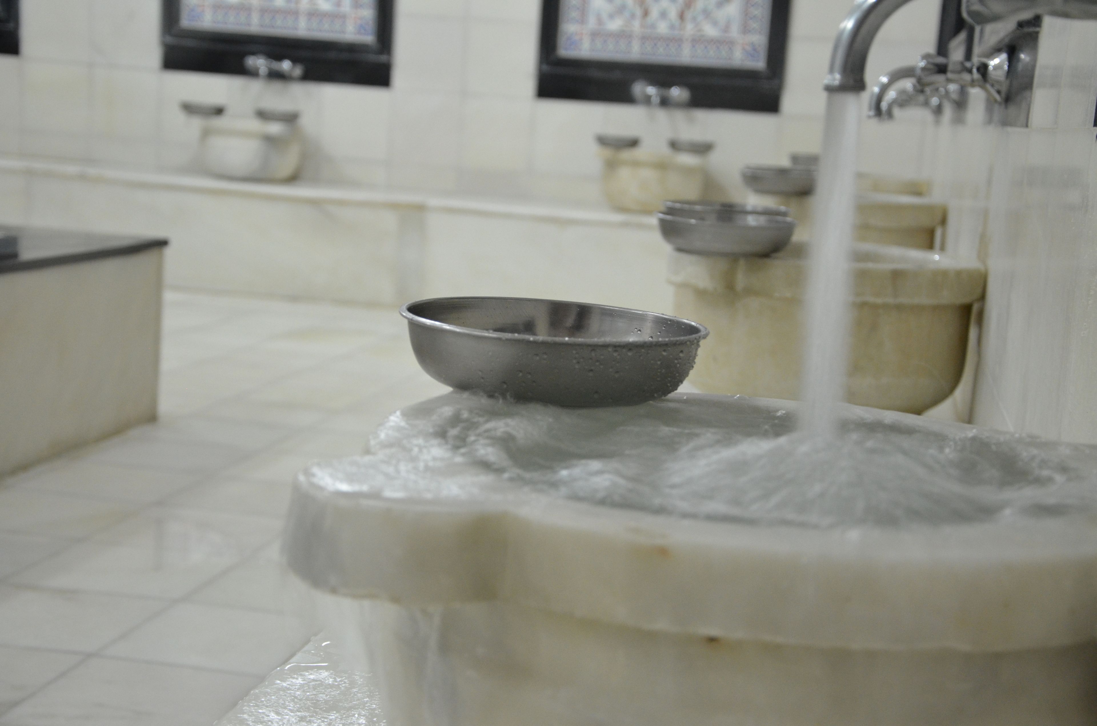 A bathroom sink with running water and a metal bowl.