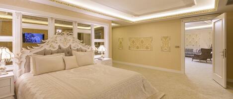 A luxurious bedroom with a large bed, ornate headboard, and a television on the wall.