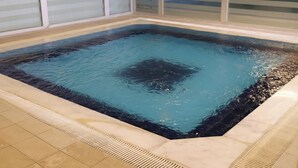 Tinaja rectangular con un interior oscuro, rodeada de un suelo de azulejos y un cerramiento de vidrio.