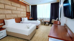 Habitación de hotel con dos camas, un escritorio, una silla, un televisor y una ventana con cortinas.