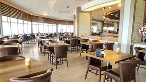 Un restaurante espacioso con numerosas mesas y sillas, amplias ventanas y una barra central.